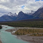 Turquoise River in Pine Forest with Mountain Peaks under Pink Sky