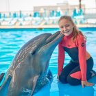 Smiling girl in pink wetsuit with friendly dolphin by pool