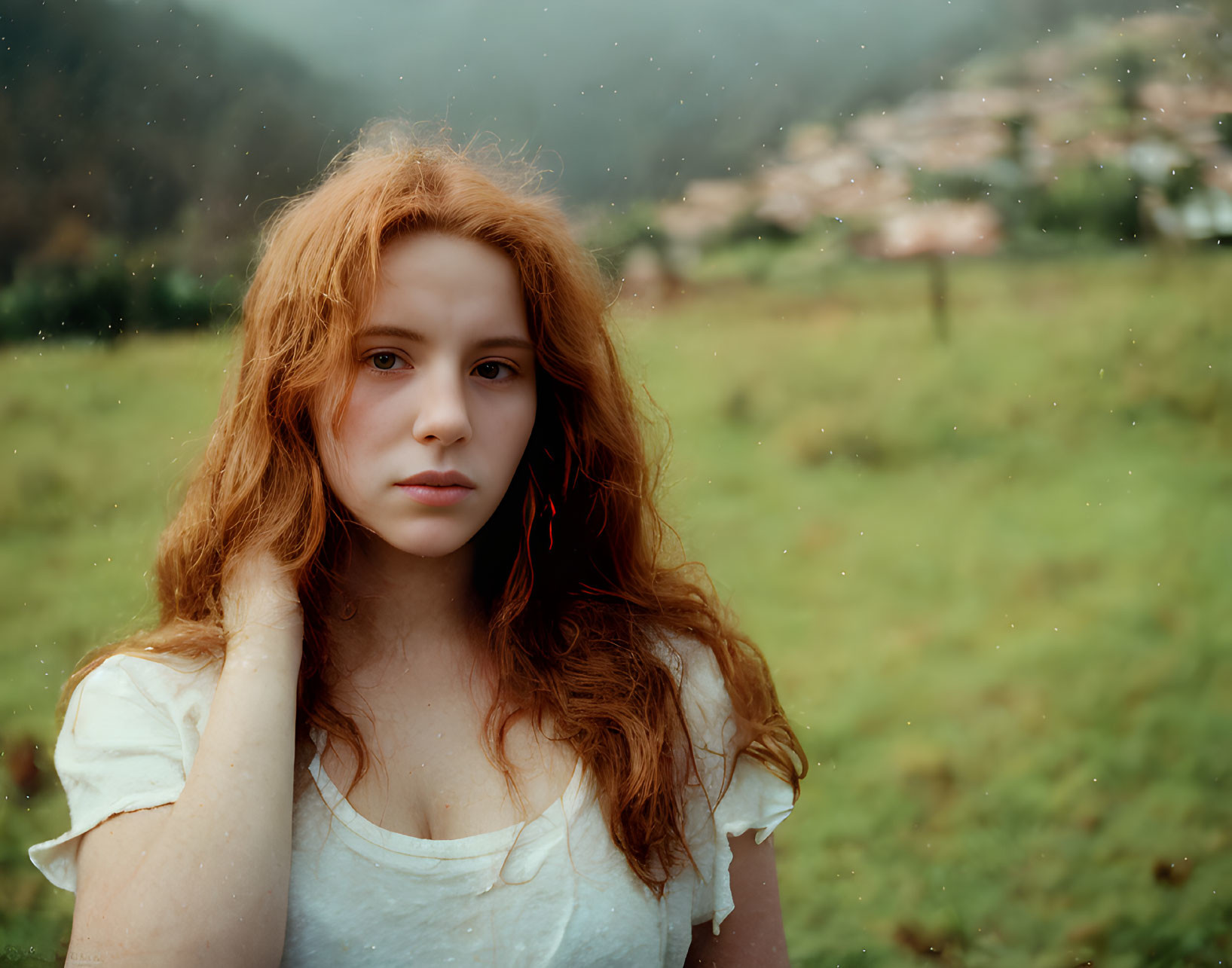 Young woman with long red hair in misty field with village background