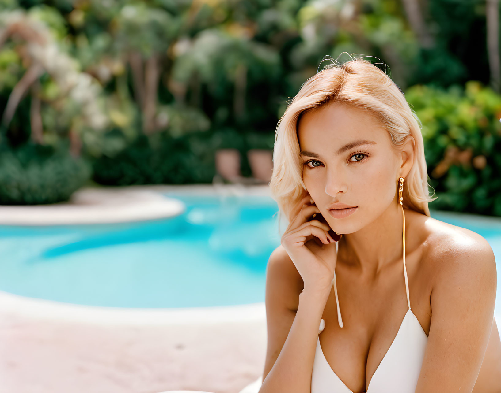 Blonde woman in white outfit with long earrings by pool