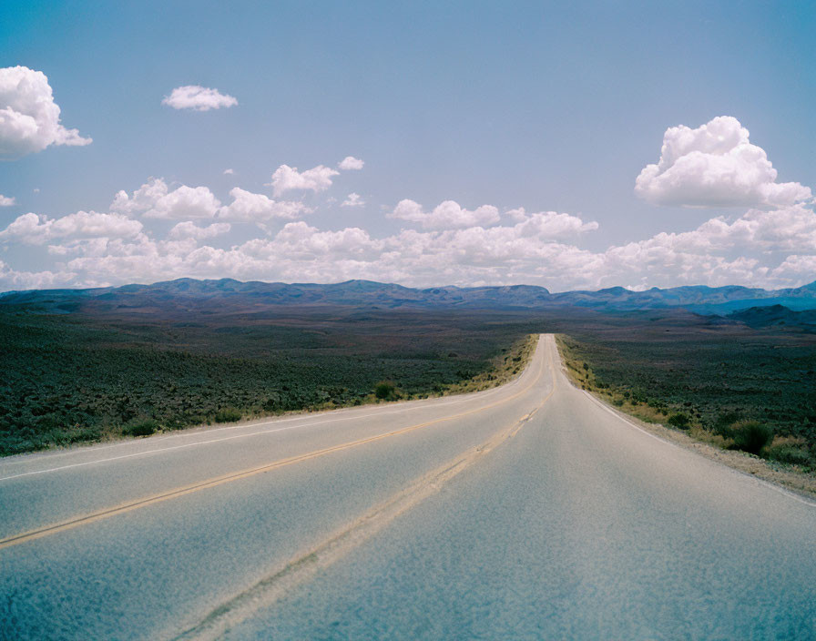 Empty straight road through arid landscape with rolling hills