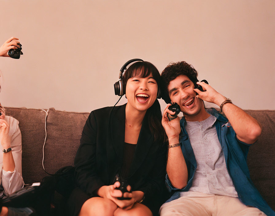 Two people smiling on a couch with gaming headsets and devices.