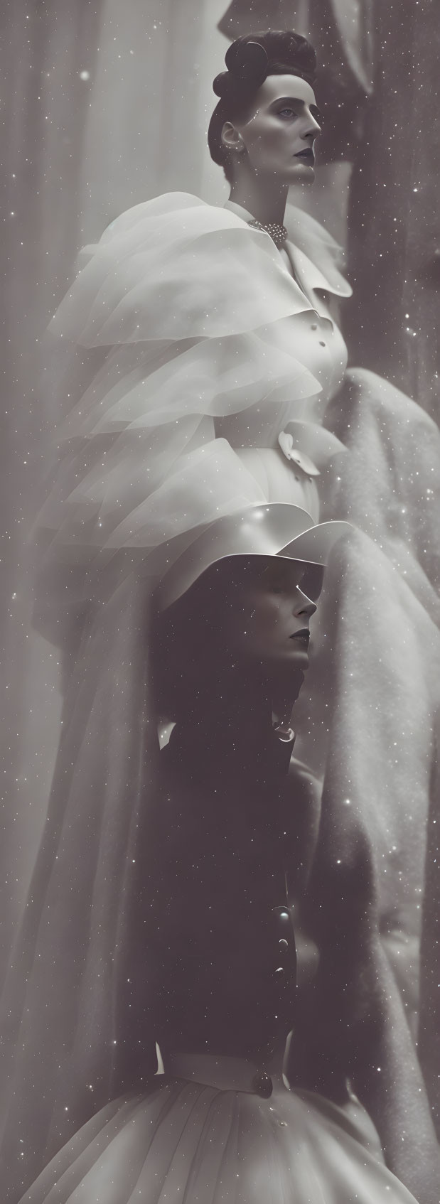 Monochromatic image of two women in elegant attire with layered ruffles posing under snowflakes