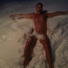 Bearded man lying shirtless in snow making snow angel