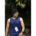 Muscular man in sleeveless top and beanie with sunglasses outdoors.