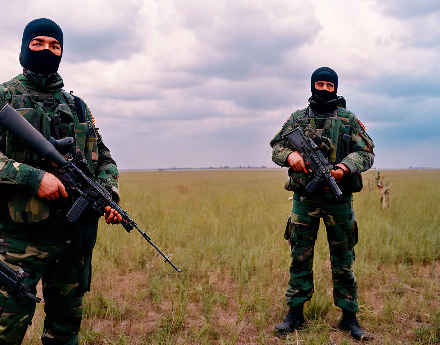 Camouflaged individuals with rifles in grassy field under cloudy sky