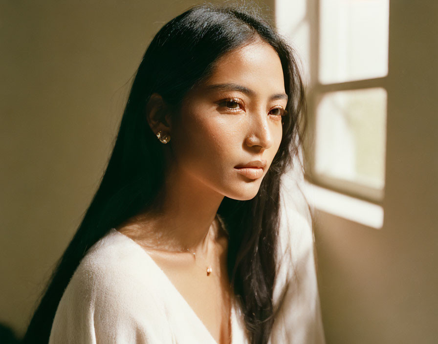 Contemplative woman in white top by window with shadows