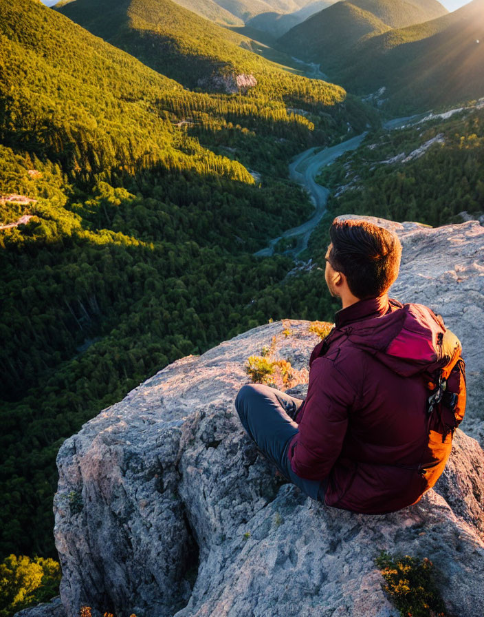 Person overlooking sunlit mountain landscape from rocky edge