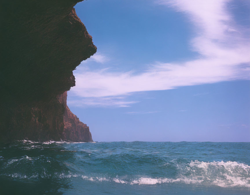 Rocky Cliff Overhangs Above Wavy Ocean