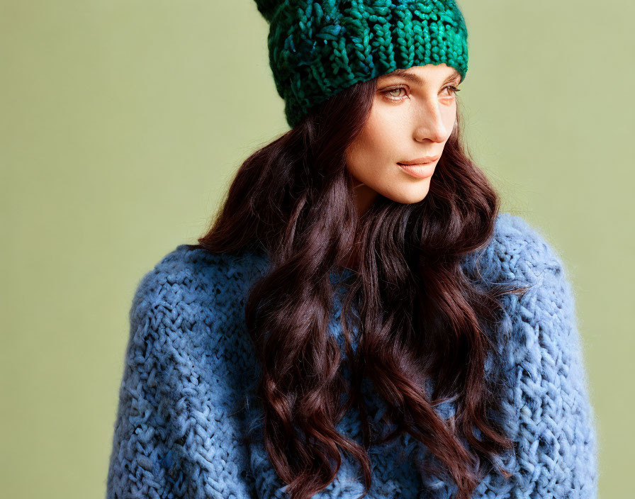 Dark-haired woman in green beanie and blue sweater on green background