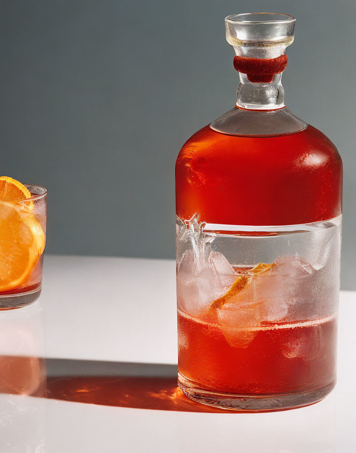 Amber liquid decanter and glass with ice and orange slice on grey background