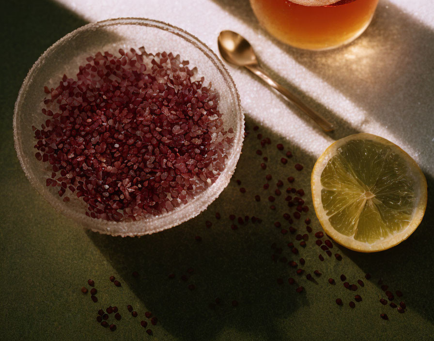 Red grains in glass bowl with lemon, golden spoon, soft shadows