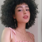 Person with Voluminous Curly Hair in Pink Ruffled Attire with Subtle Makeup