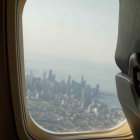 Child in beanie gazes at city skyline from airplane window