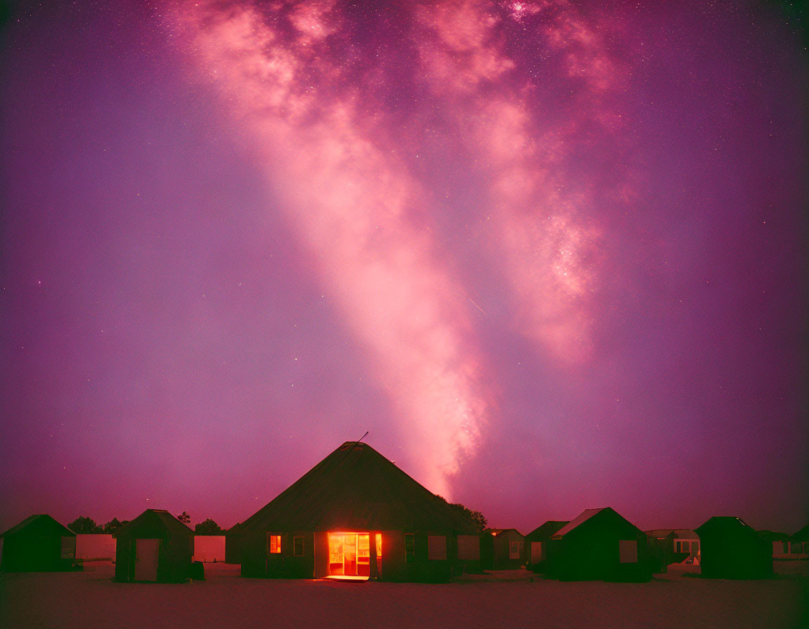 Silhouette of cottage under starry night sky with Milky Way and warm glow