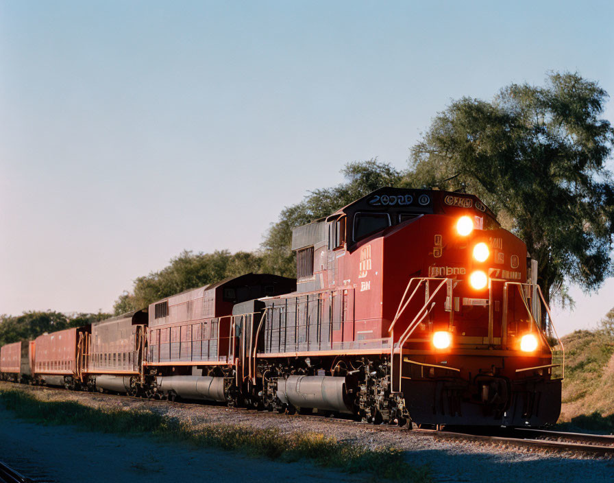 Red locomotive leads freight train through rural landscape