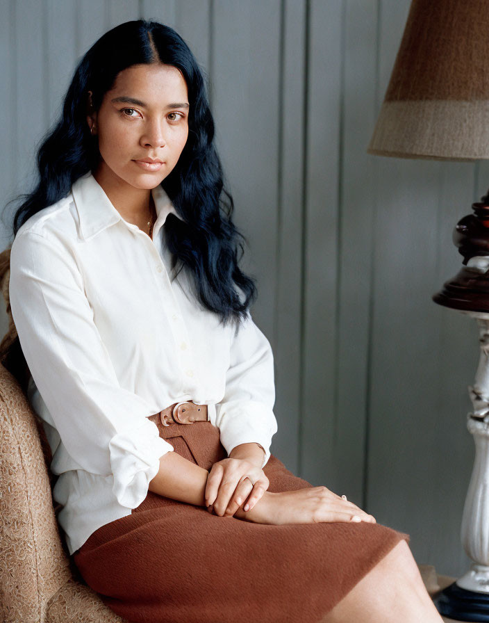 Woman with Long Dark Hair in White Shirt and Tan Skirt Against Grey Backdrop