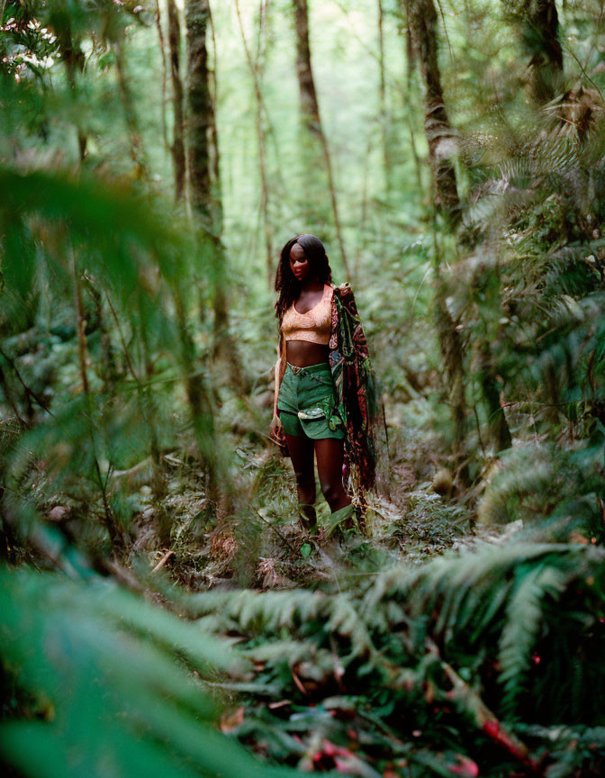 Woman in bralette and shorts surrounded by lush greenery holding fabric