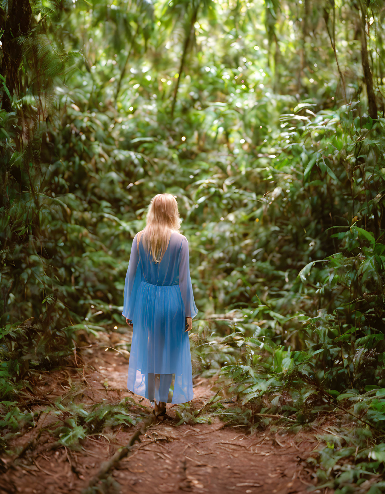 Woman in Blue Dress Standing on Forest Path surrounded by Green Foliage