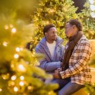 Elderly couple in festive attire by Christmas tree with gifts and drink