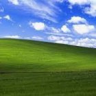 Person standing amidst rolling green hills under blue sky.