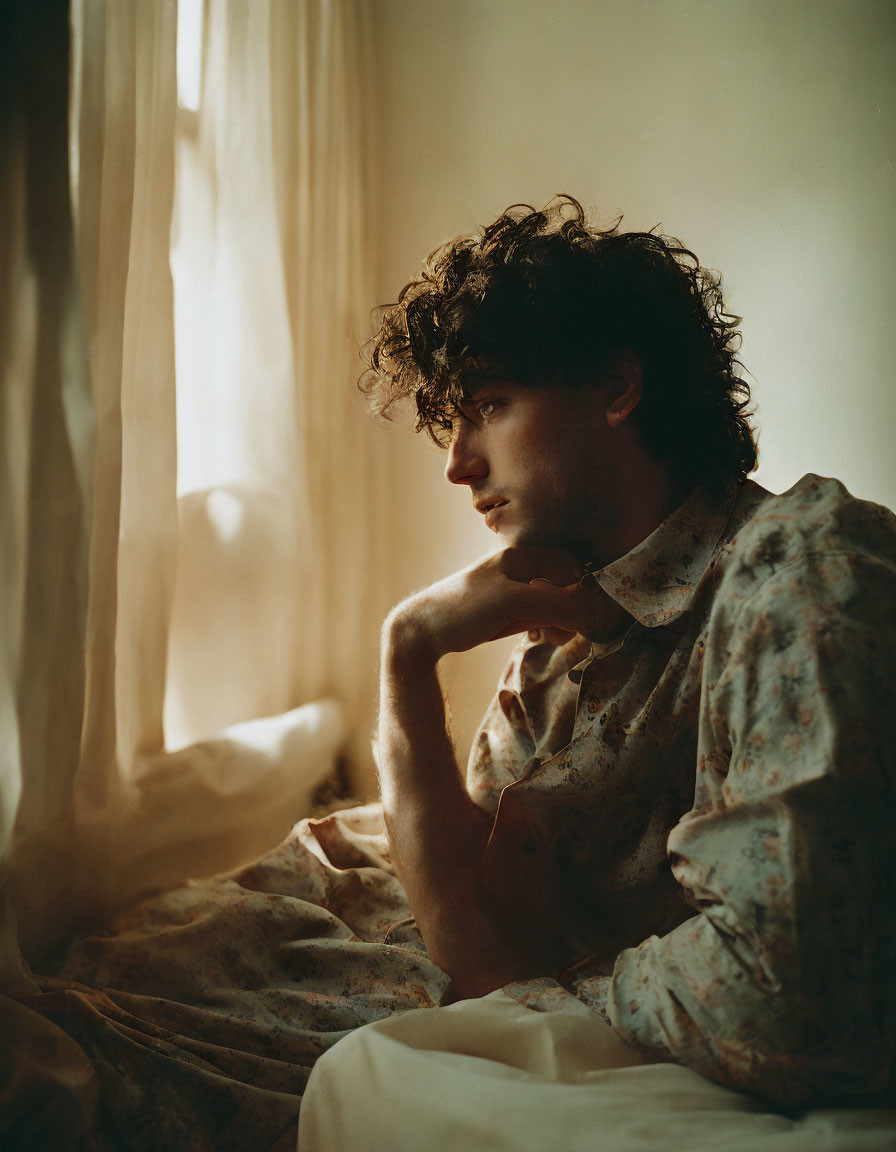 Curly-Haired Man Contemplating by Sheer-Curtained Window