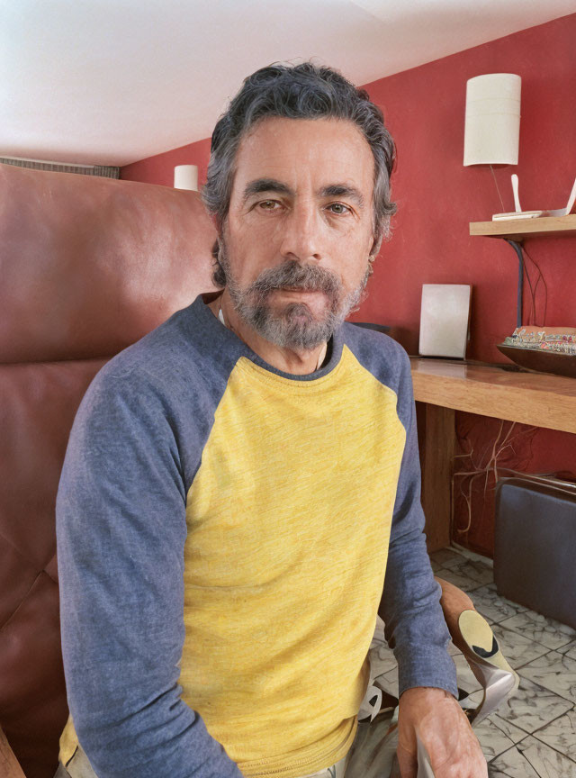 Salt-and-Pepper-Haired Man in Yellow and Blue Sweater on Red Wall Background