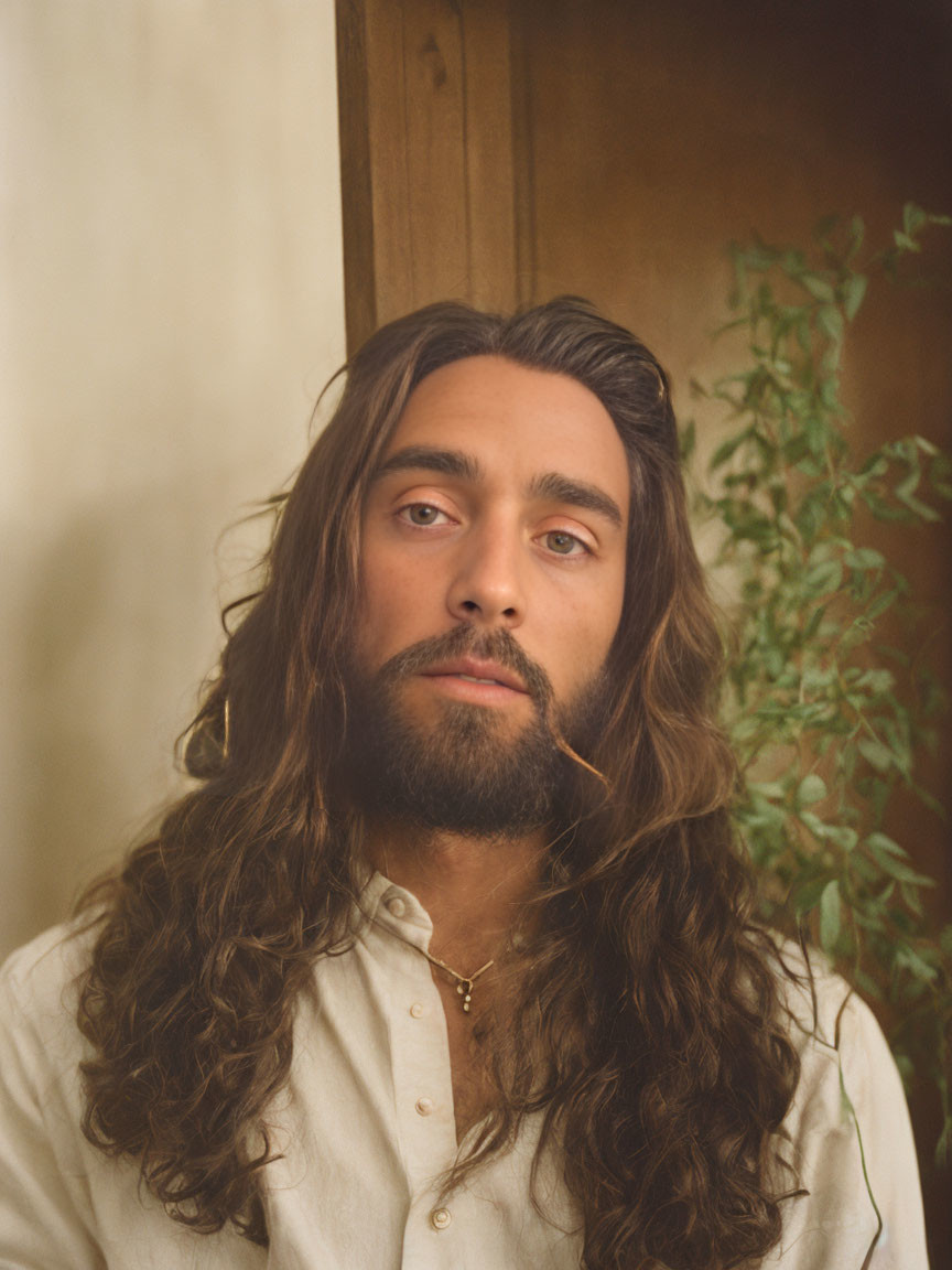 Bearded man in cream shirt with curly hair, plant background