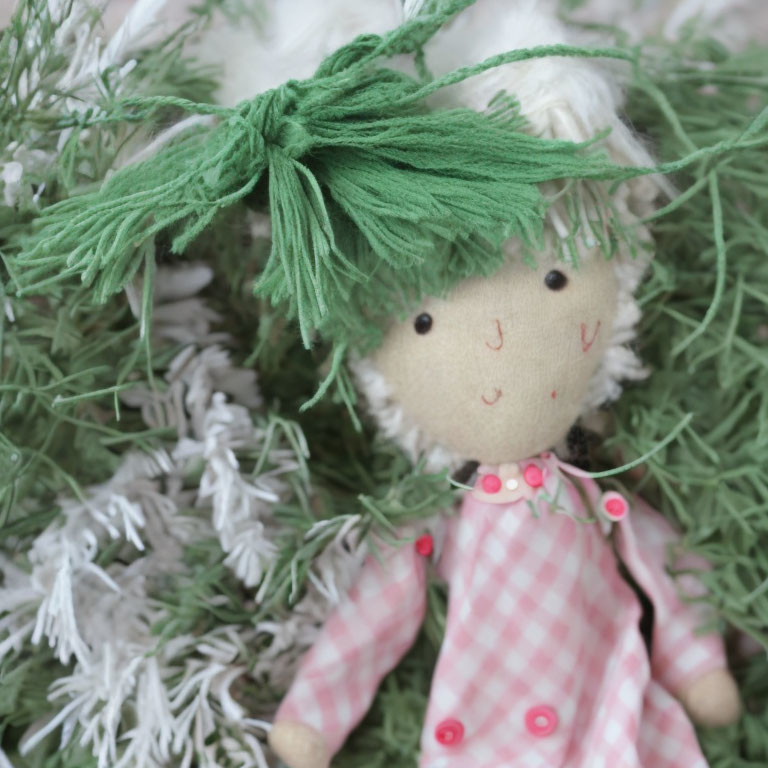 Handmade doll with green yarn hair and pink checkered dress among festive decorations