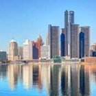 Golden sunlight illuminates futuristic city skyline with skyscrapers reflected in tranquil water under clear blue sky