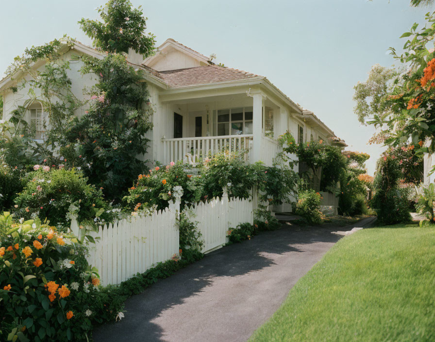 White house with picket fence, landscaped garden, and paved pathway under clear sky