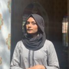 Woman in patterned headscarf and white top gazes at sunlit old buildings