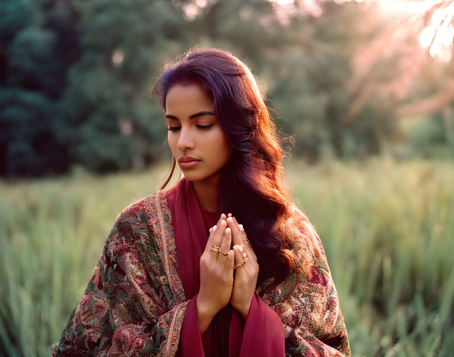 Woman in prayer pose in maroon dress among tall green grass