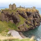 Castle-like structure on rocky outcrop by lush sea.