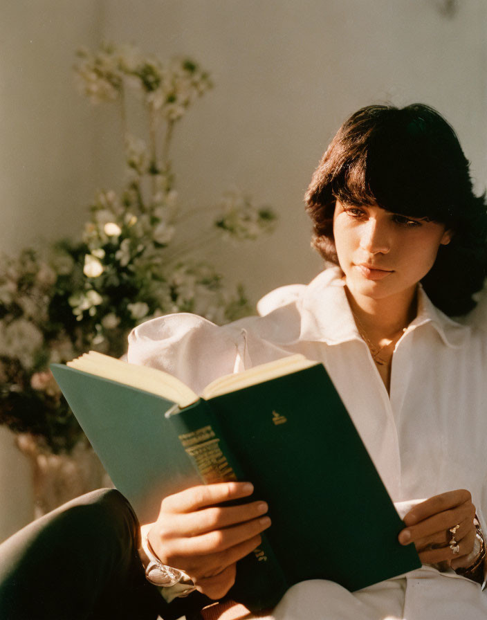 Person in white shirt reading book with sunlight and flowers in background