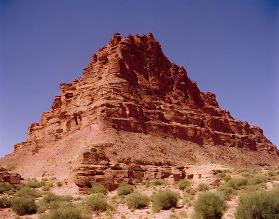 Rugged red rock formation in desert landscape with green shrubbery