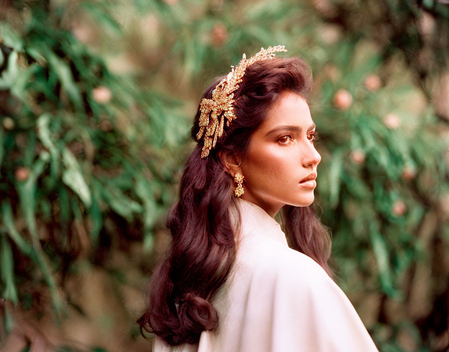 Dark-haired woman in golden headpiece gazes thoughtfully amidst lush greenery