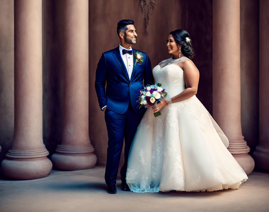 Elegantly dressed couple in blue suit and bridal gown with flowers