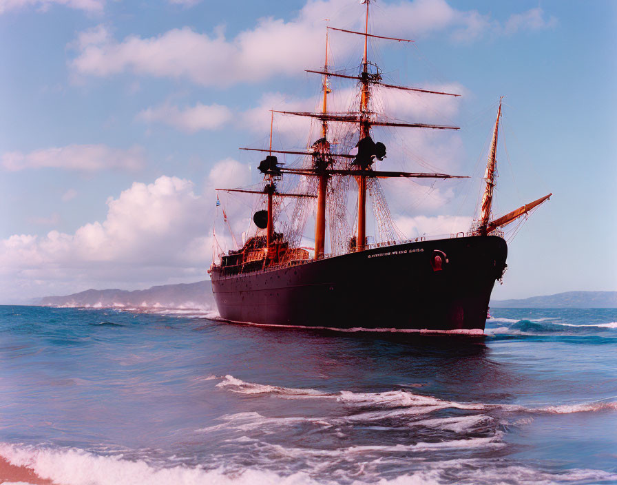 Vintage tall ship with multiple masts near beach under blue skies