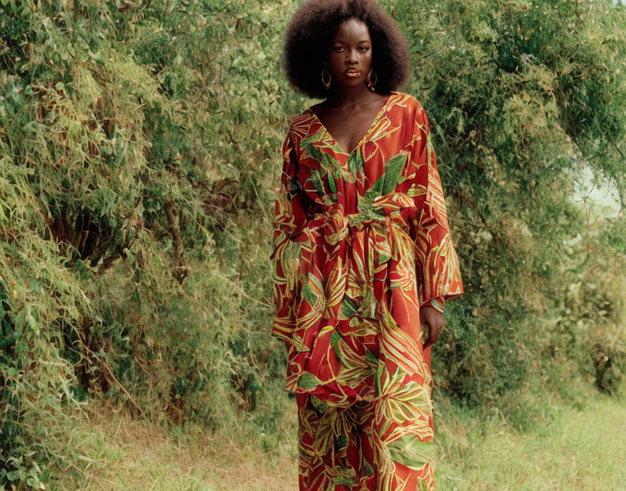 Woman in vibrant red floral dress among lush greenery with natural afro hairstyle
