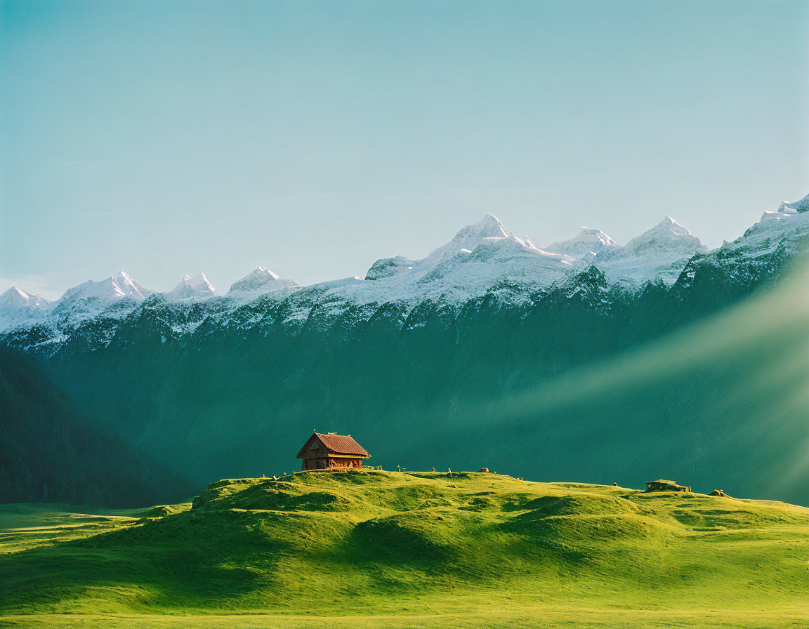 House on lush green hill with snow-capped mountains and clear blue sky