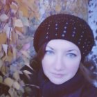 Brown-haired woman in purple scarf with blue eyes, surrounded by red autumn leaves