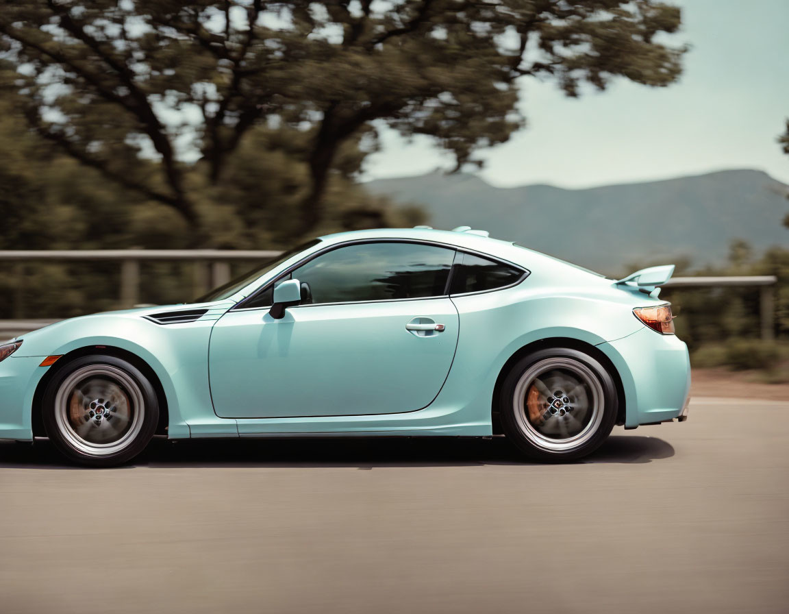 Pastel blue sports car with large rear spoiler on road with trees and mountains