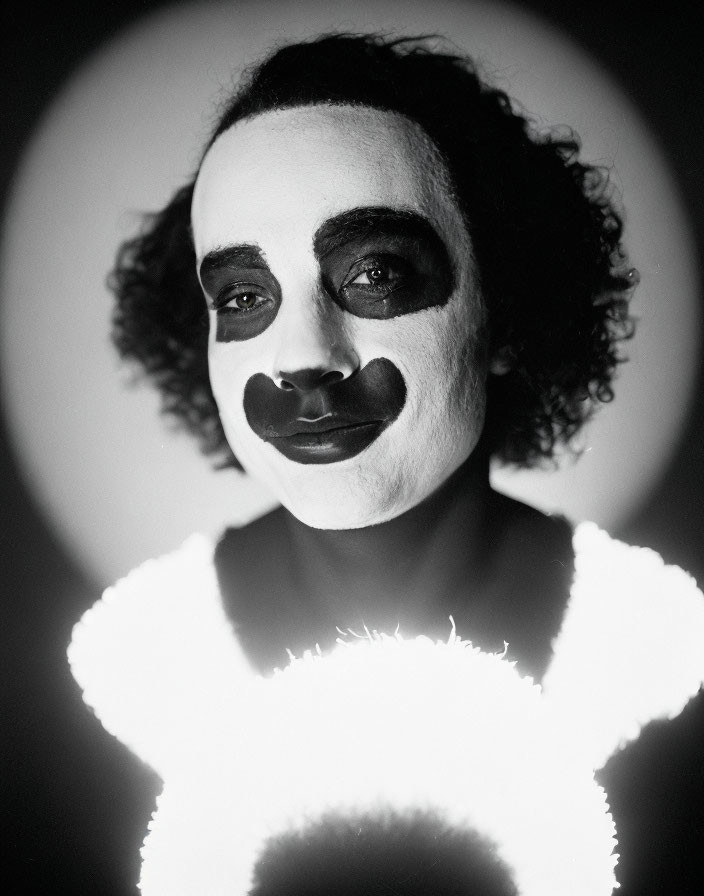 Monochrome portrait of person with dramatic clown makeup and backlit glow