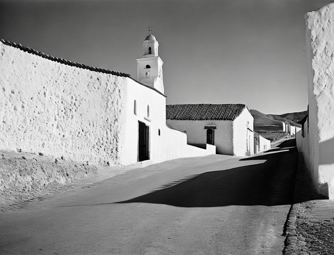 Monochrome photo: Sunlit street with white buildings and church.