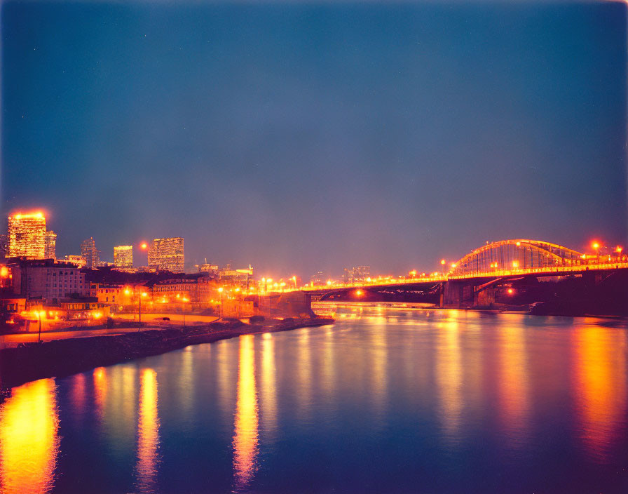 Night cityscape with illuminated buildings, lit bridge, and dusky sky