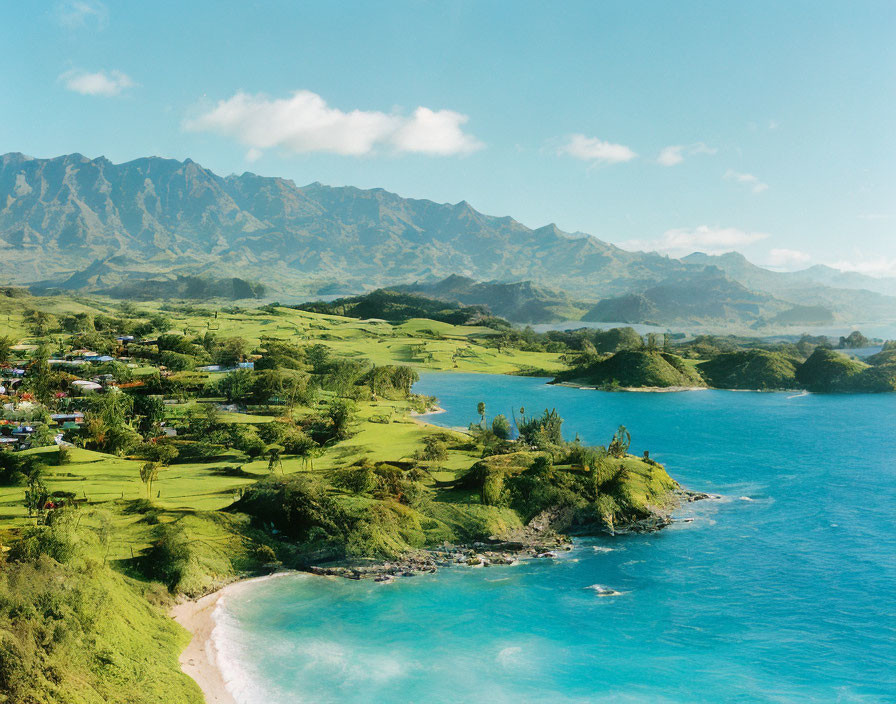 Scenic coastal landscape: green hills, blue ocean, sandy beach, rugged mountains