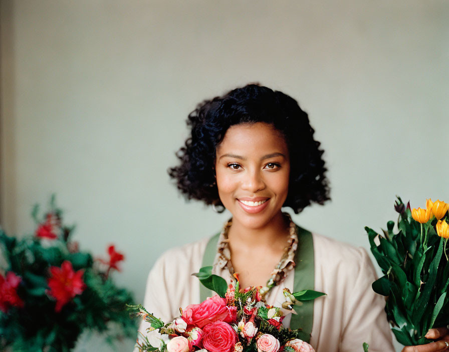 Smiling woman with curly hair holding flowers in beige top