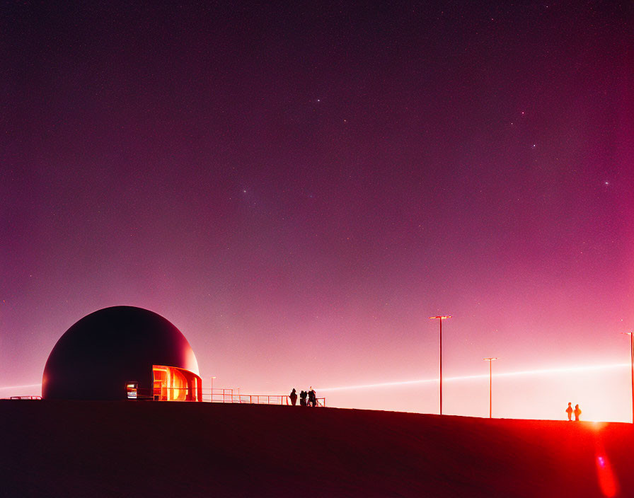 Dome structure glowing at night with people under starry sky