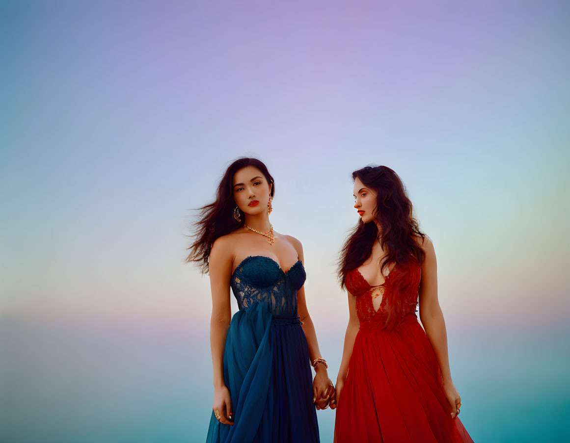 Two women in elegant blue and red gowns holding hands at dusk